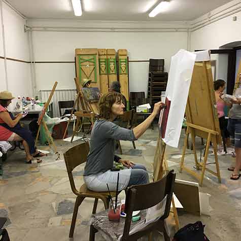 Fotografija prikazuje udeležence poletne slikarske delavnice med ustvarjalnim slikarskim delom. 