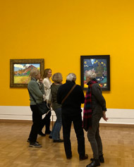 Fotografija prikazuje udeležence slikarskega tečaja, ki si z velikim navdušenjem ogledujejo slike Paul Gauguina na razstavi v Kunstforum, Dunaj, januar 2025.